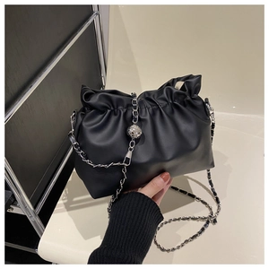 Detail of black pleated bucket bag with silver chain strap and metal ball accessory