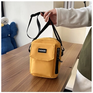 Close-up of yellow nylon crossbody bag with fashion label and adjustable black strap