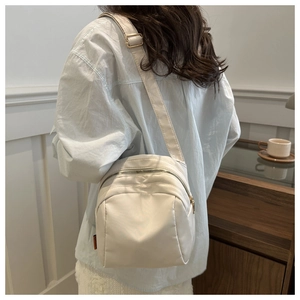 Détail du sac bandoulière beige en toile avec fermetures éclair et bandoulière réglable