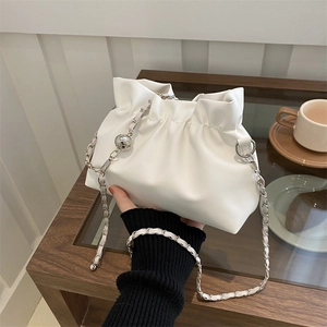Elegant white pleated cloud pouch bag with silver chain strap shown in a cafe setting