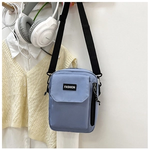 Detail of light blue nylon crossbody bag featuring a front pocket and adjustable strap