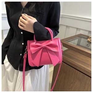 Close-up of bright pink square handbag with bow design and adjustable shoulder strap