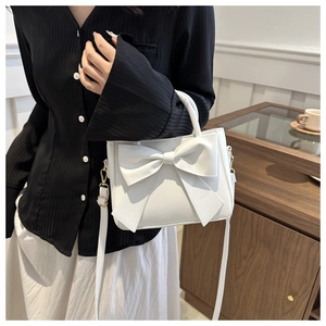 Mini borsa bianca chic con grande fiocco indossata da modella in camicia nera plissettata
