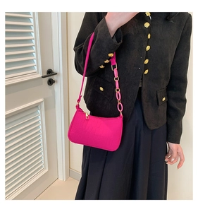 Detail of rose red faux leather baguette bag with crocodile texture and acrylic chain link