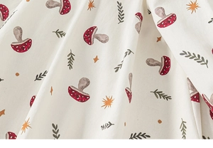 Nahaufnahme des Baumwollstoffes mit roten Pilzmustern und grünen Blättern am Kleid