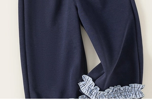 Detail shot of navy blue toddler trousers featuring ruffled blue and white gingham cuffs