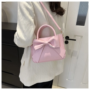 Detail of a pink crossbody bag featuring a large bow design and a slim leather strap