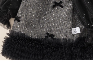 Detail of tweed dress fabric with velvet bow and multi-layered black mesh pleated hem