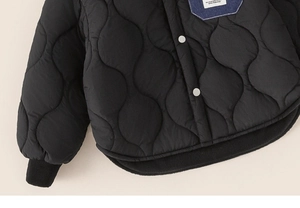 Detail of black quilted boy jacket with silver snaps and a denim patch pocket