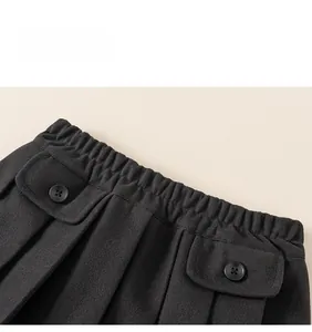 Detail of children's black pleated skirt featuring elastic waistband and buttoned pockets