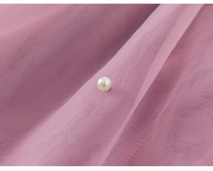 Close-up of pink mesh fabric featuring a delicate white pearl and fine honeycomb texture