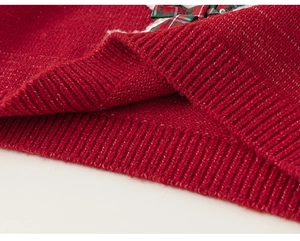 Close-up of red knit sweater featuring ribbed cuffs and festive plaid bow detail