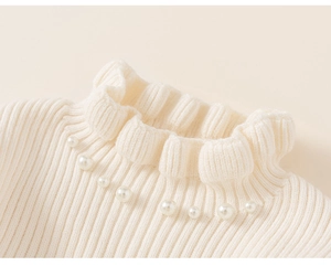 Detail of cream knit sweater showing ruffled neckline and pearl embellishments