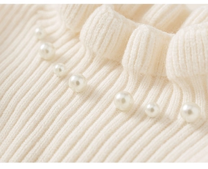 Detailed macro view of cream knit fabric with ribbed texture and elegant pearl embellishments