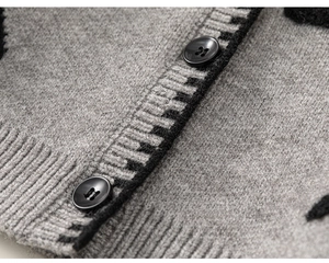 Detail van grijs gebreid vest met zwarte geometrische patronen en ronde knopen