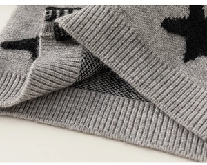 Detailopname van de grijze gebreide trui met zwarte ster jacquard en een geribbelde manchet