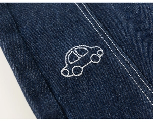 Detail van donkerblauwe denim stof met witte stiksels en een klein geborduurd autootje