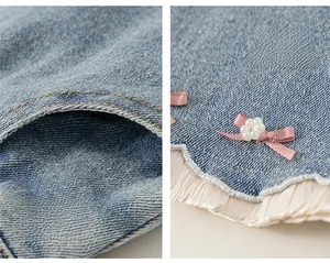 Détail du pantalon en jean bleu avec nœud rose perlé et bordure en mousseline blanche