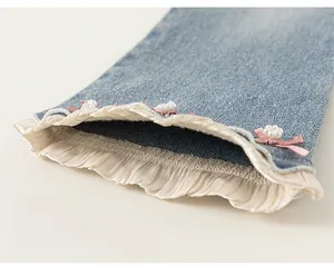 Détail du jean évasé fille montrant dentelle, nœud rose et accents de perles