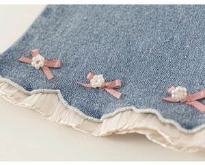 Détail du pantalon en jean fille avec nœud rose, perles et ourlet à volants plissés