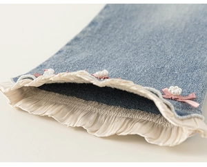 Détail de l'ourlet en jean avec dentelle crème et nœud en ruban rose orné de perles