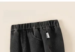 Detail of high-waisted elastic waistband on dark grey denim jeans with bow embroidery