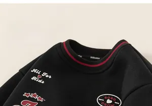 Détail du sweat-shirt noir pour enfant avec col rayé et broderie blanche sur le devant