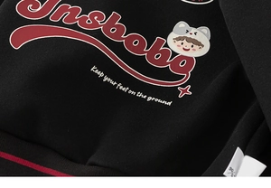 Détail du sweat-shirt noir en coton montrant la broderie Unsbobo et le bord du col rayé