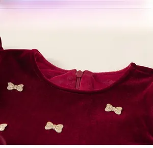 Détail d'un col en velours rouge avec des nœuds à paillettes dorées et un zip invisible