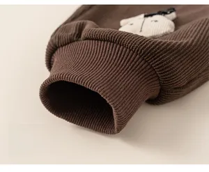 Détail d'un pantalon enfant en velours marron chaud avec poignets côtelés et écusson