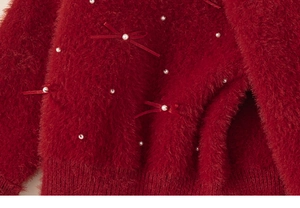 Detail of red faux fur sweater featuring white pearls and elegant velvet bows