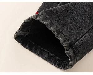 Macro shot of girls dark denim trousers featuring detailed red bow embroidery on the hem