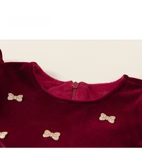 Détail de robe de fille en velours bordeaux avec nœuds dorés et fermeture invisible