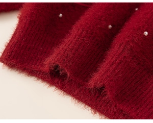 Detailed close-up of red mink velvet knit sweater featuring white pearls and ribbed hem