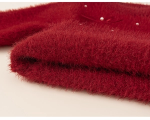 Close-up of red plush knit girl's sweater fabric with delicate white pearl accents