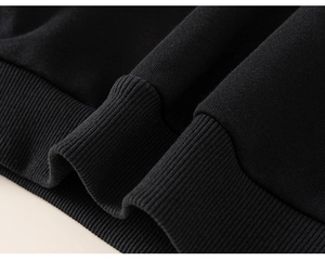 Detailed close-up of premium black knit fabric and elastic ribbed hem on a kids sweatshirt