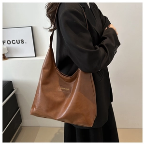 Detailed close-up of brown PU leather tote bag with fashion label on black blazer