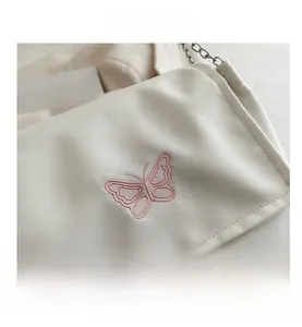 Detail of pink butterfly embroidery on off-white canvas bag with silver chain