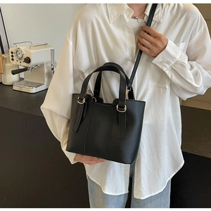 Dettaglio di una borsa a secchiello in pelle nera con finiture dorate e tracolle fini