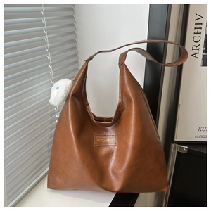 Close-up of brown textured leather tote bag with white fluffy pompom charm detail