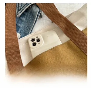 Détail du cabas en toile avec poche avant, poignée tressée marron et étiquette en cuir mode