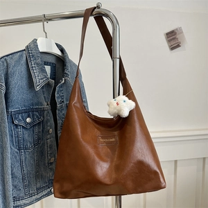 Brown leather large tote bag with star charm and fashion label shown on a blue jacket