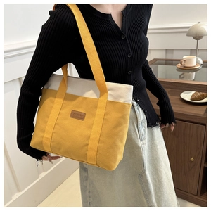 Détail du sac cabas en toile montrant des coutures contrastées jaune et beige et étiquette mode