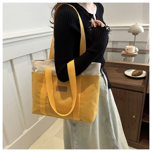 Vue latérale d'un grand sac cabas en toile jaune et crème porté à l'épaule dans une pièce