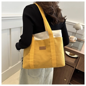 Détail du sac fourre-tout en toile jaune et beige avec patch en cuir et large bandoulière