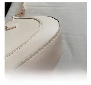 Detailed close-up of fine stitching and gold hardware on a cream crescent handbag