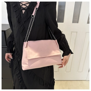 Pink crossbody bag with chain strap and butterfly embossing worn by a model in black dress