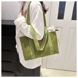 Gros plan sur le sac fourre-tout en toile verte et beige avec écusson en cuir sur modèle