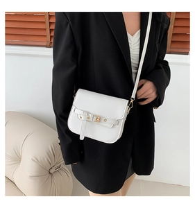 Detail einer weißen Leder-Satteltasche mit goldener Schnalle an einem Model im schwarzen Blazer