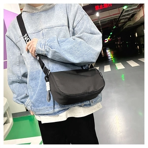 Détail du sac bandoulière noir en nylon avec sangle large imprimée de texte NONE